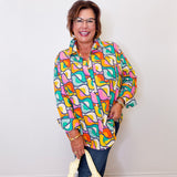 Woman wearing a colorful patterned shirt holding a yellow bag against a white wall.