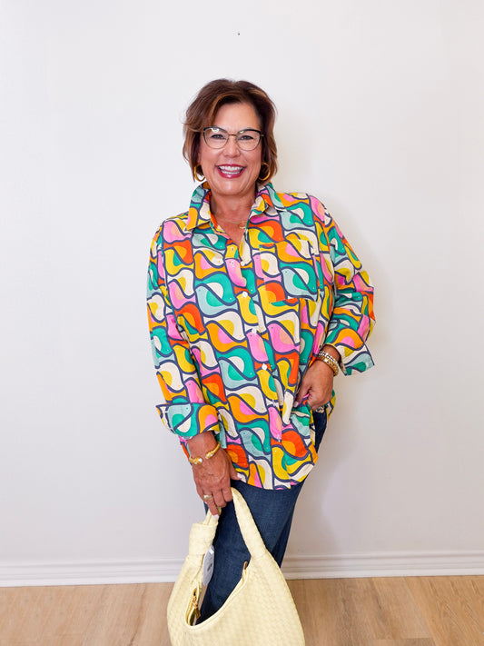 Woman wearing a colorful patterned shirt holding a yellow bag against a white wall.