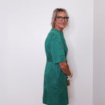 Woman wearing a green dress standing against a white wall.
