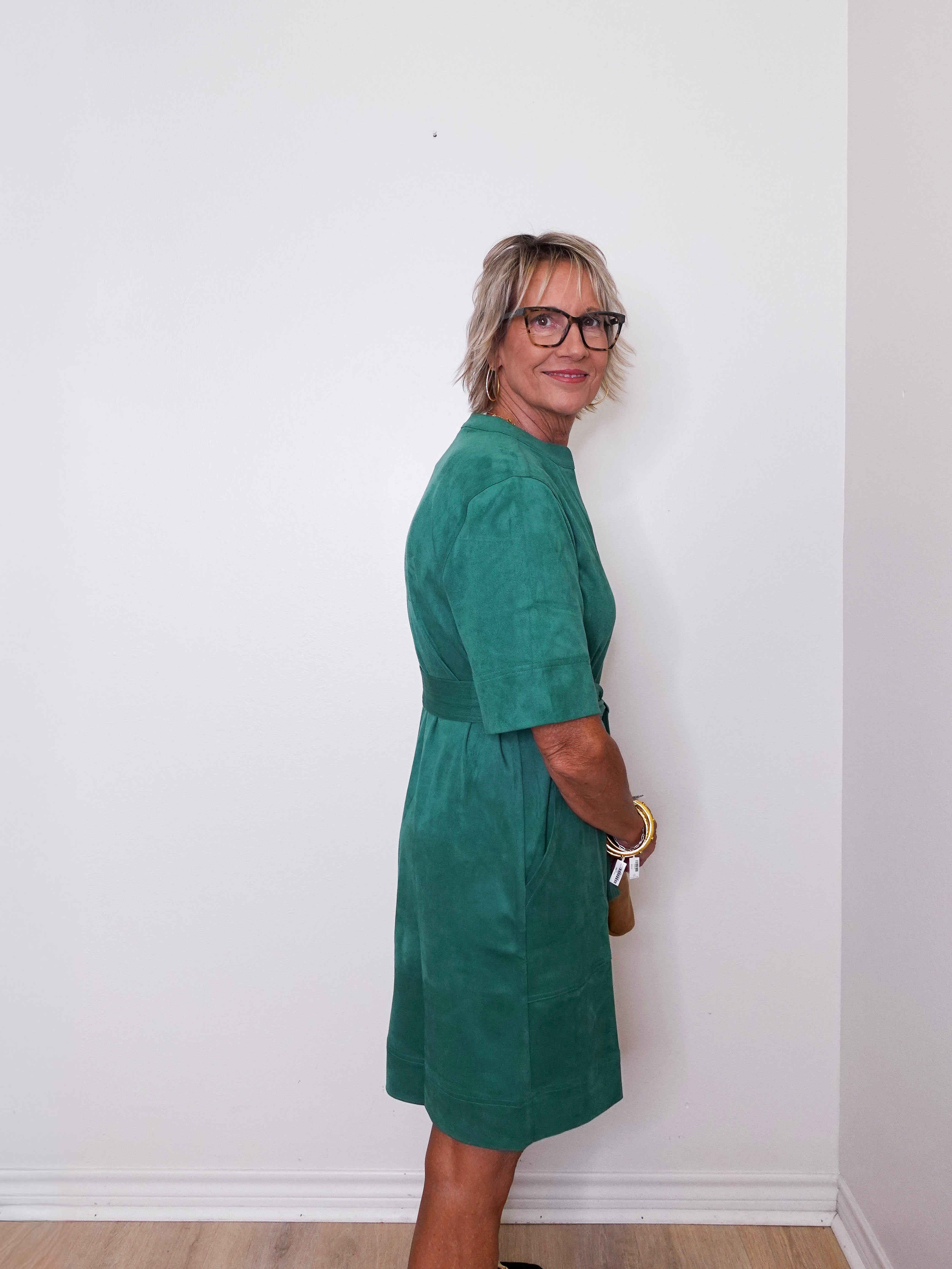 Woman wearing a green dress standing against a white wall.