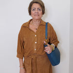 Woman in a brown outfit holding a blue bag against a white background