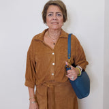 Woman in a brown outfit holding a blue bag against a white background