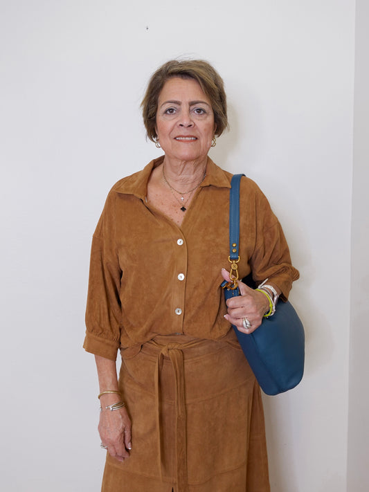 Woman in a brown outfit holding a blue bag against a white background