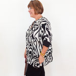 Woman wearing a black and white patterned blouse against a white background