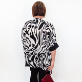 Person wearing a black and white patterned top holding a red handbag against a white wall.