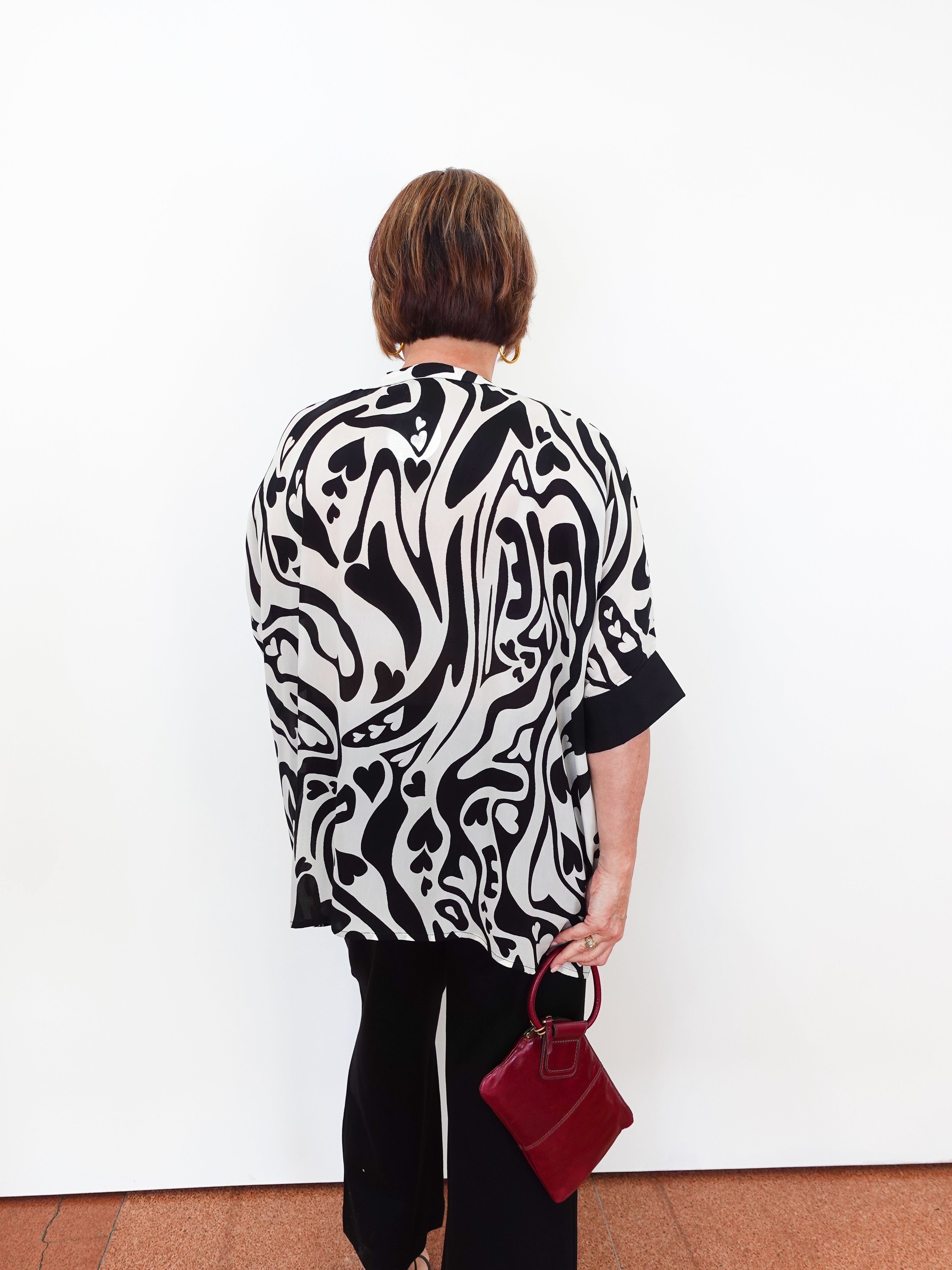 Person wearing a black and white patterned top holding a red handbag against a white wall.