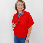 Woman wearing a red sweater and blue jeans, holding glasses, on a white background