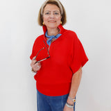 Woman wearing a red sweater and blue jeans, holding glasses, on a white background