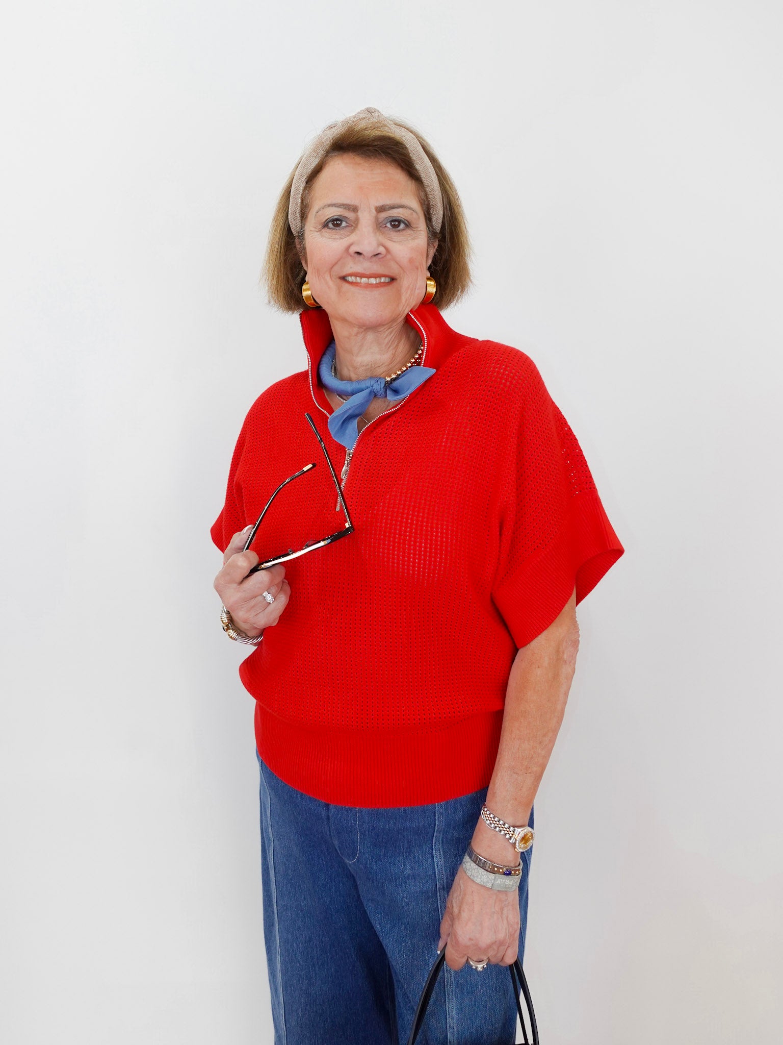 Woman wearing a red sweater and blue jeans, holding glasses, on a white background