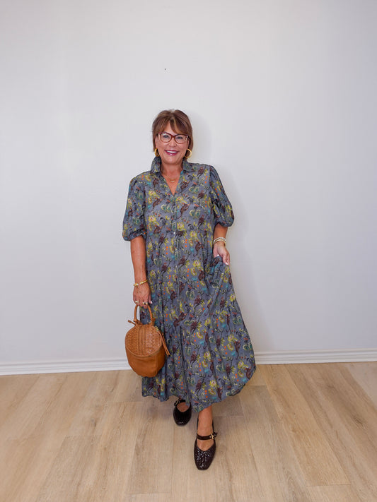 Woman wearing a floral dress holding a brown handbag against a white wall.