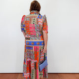 Person wearing a colorful patchwork dress with a white wall background