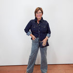 A woman modeling a dark navy blue denim shirt and patterned wide-leg pants with a blue and beige animal print, standing against a plain white wall.