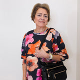 Woman wearing a colorful floral top holding a black handbag against a white background