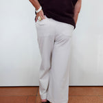 A person shown from the back wearing light beige wide-leg cropped pants, a dark ribbed sleeveless top, and black high heels against a plain white wall and terracotta floor.