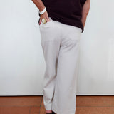 A person shown from the back wearing light beige wide-leg cropped pants, a dark ribbed sleeveless top, and black high heels against a plain white wall and terracotta floor.