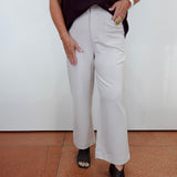 A person wearing light beige wide-leg cropped pants, a dark burgundy ribbed short-sleeve top, and black peep-toe heels, standing against a white wall with terracotta tiled flooring.