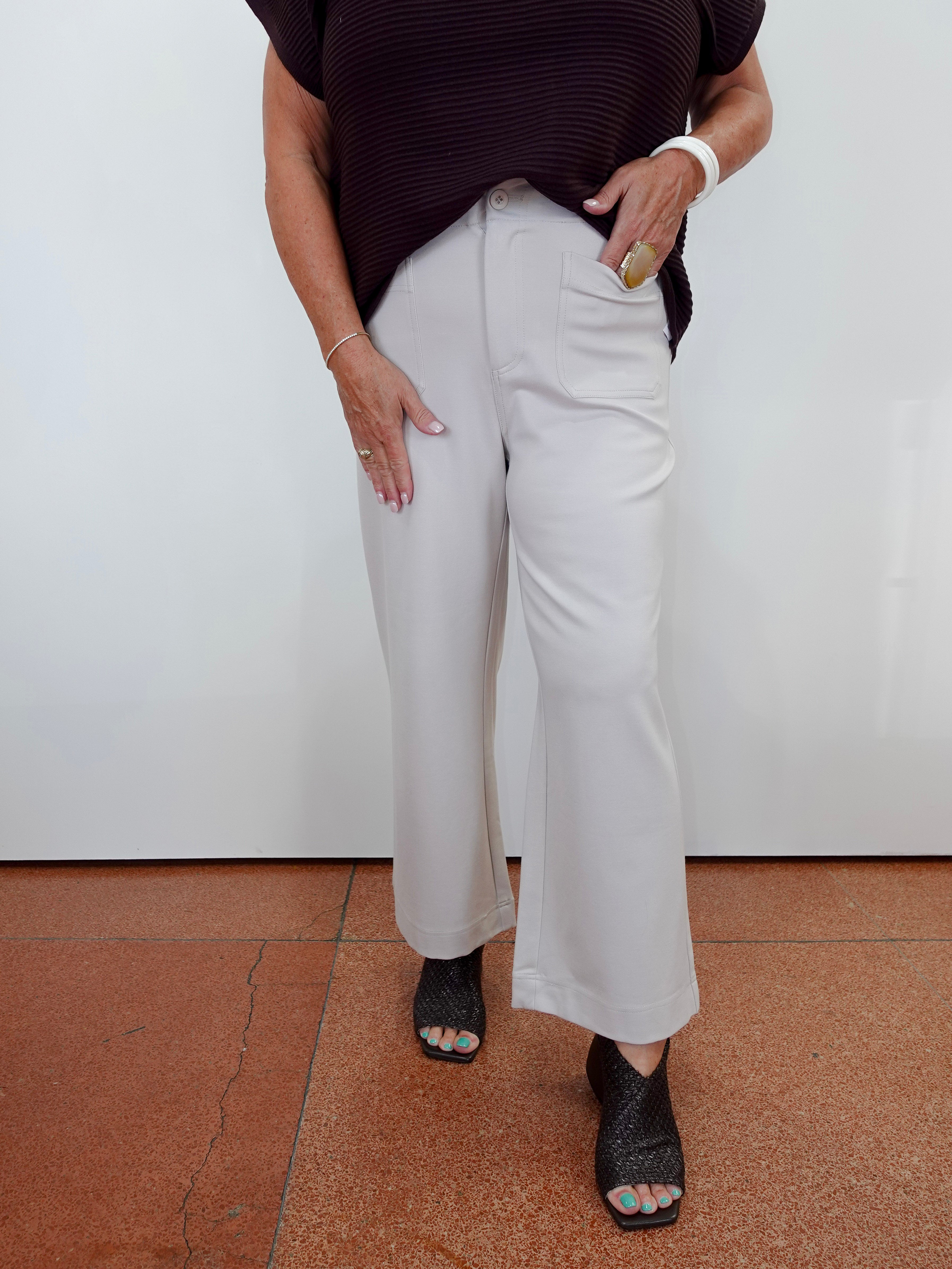 A person wearing light beige wide-leg cropped pants, a dark burgundy ribbed short-sleeve top, and black peep-toe heels, standing against a white wall with terracotta tiled flooring.