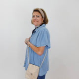 Woman wearing a blue shirt and jeans, holding a beige bag against a white background