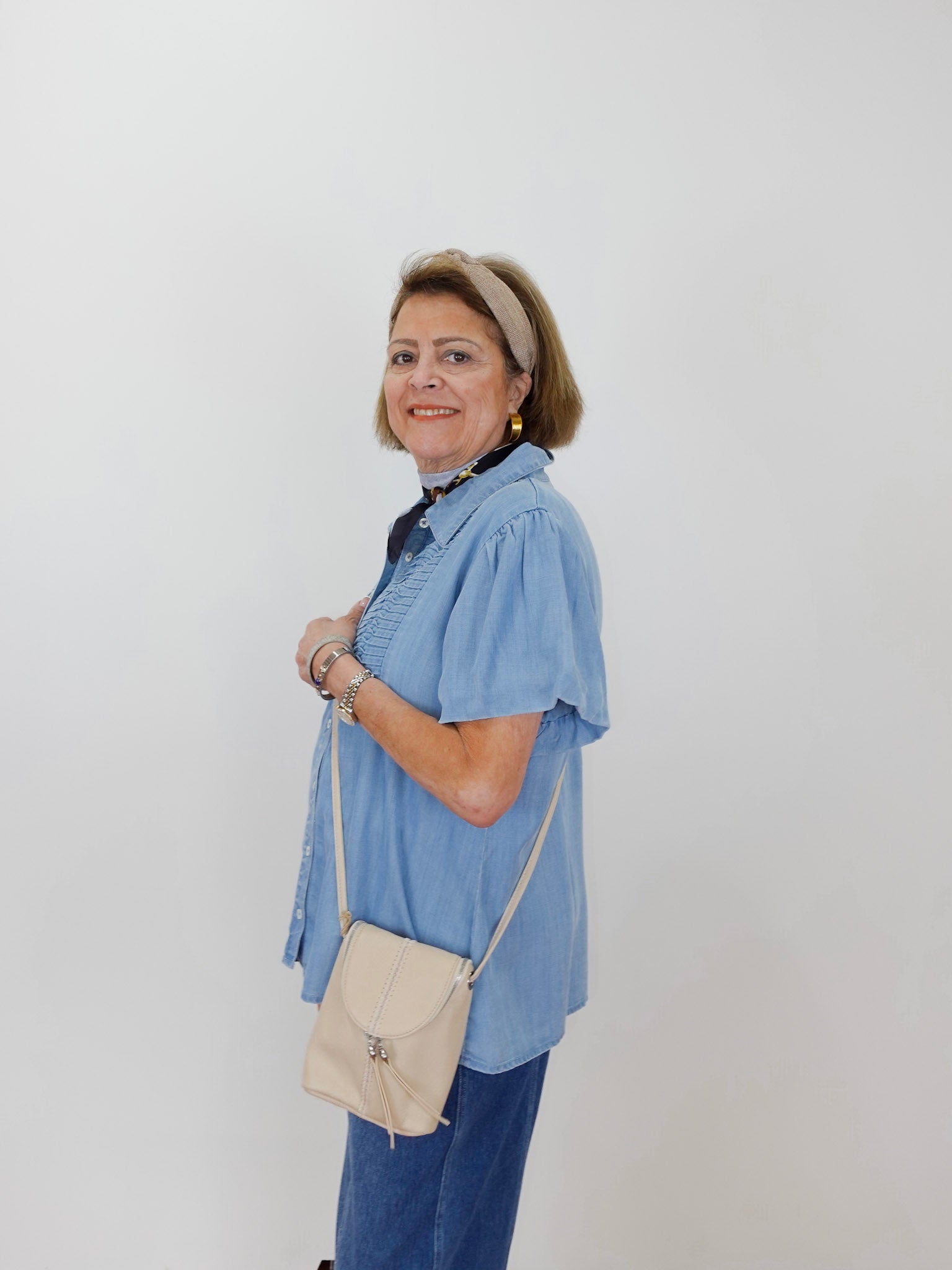 Woman wearing a blue shirt and jeans, holding a beige bag against a white background