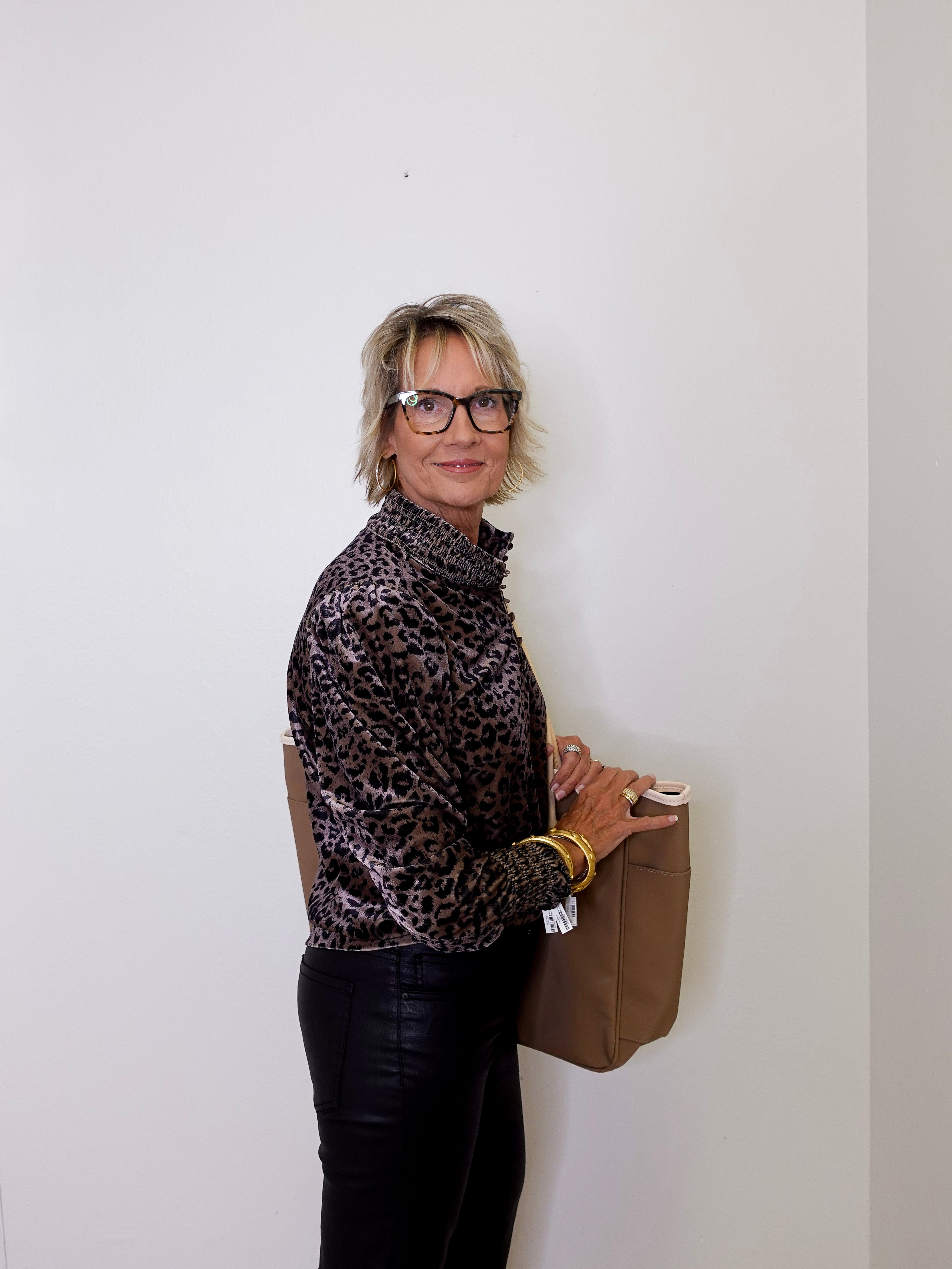 Person wearing a leopard print shirt and holding a brown bag against a white wall