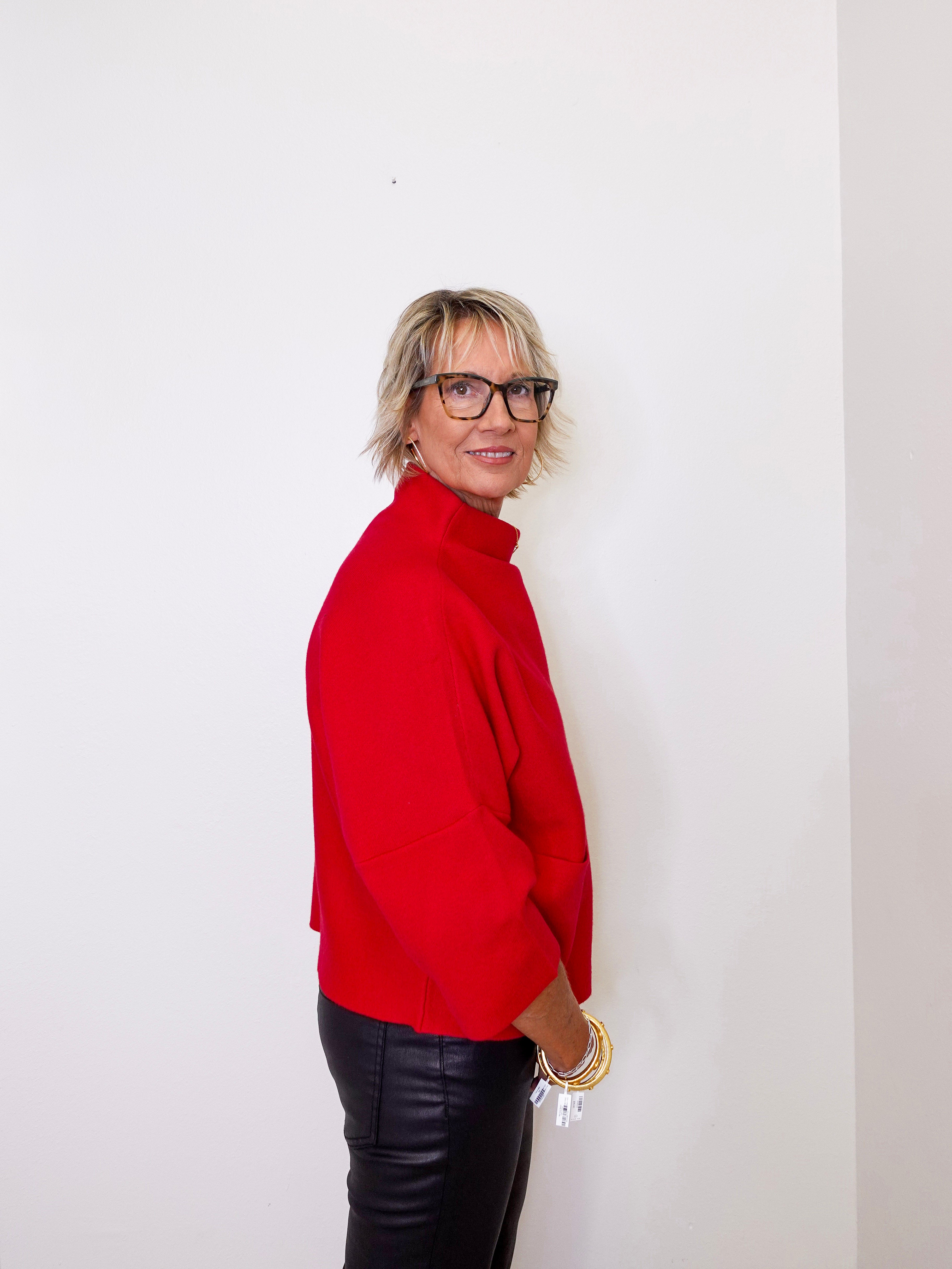 Woman wearing a red sweater and black leather pants against a white background