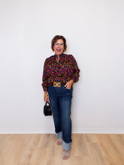 Woman wearing a colorful blouse and blue jeans against a white wall.