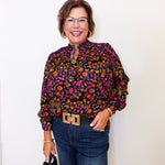 Woman wearing a colorful patterned blouse and jeans against a white background