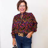 Woman wearing a colorful patterned blouse and jeans against a white background