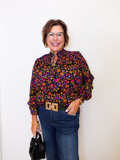 Woman wearing a colorful patterned blouse and jeans against a white background