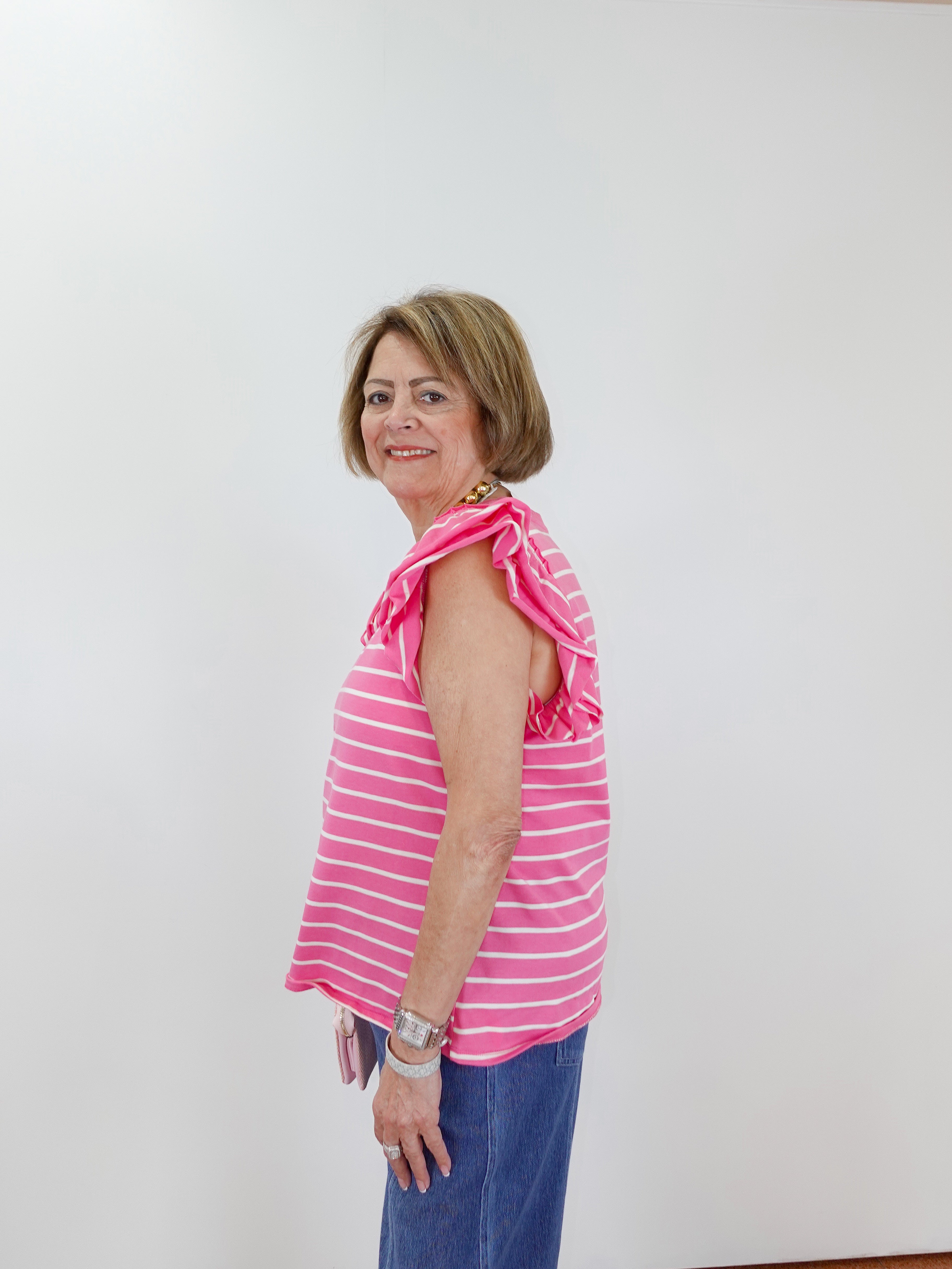 Woman wearing a pink striped sleeveless top and blue pants against a white background