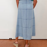 Person wearing a blue denim skirt and green top on a plain background