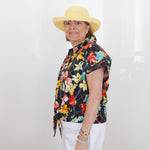 Person wearing a colorful floral shirt and white pants with a straw hat against a plain background