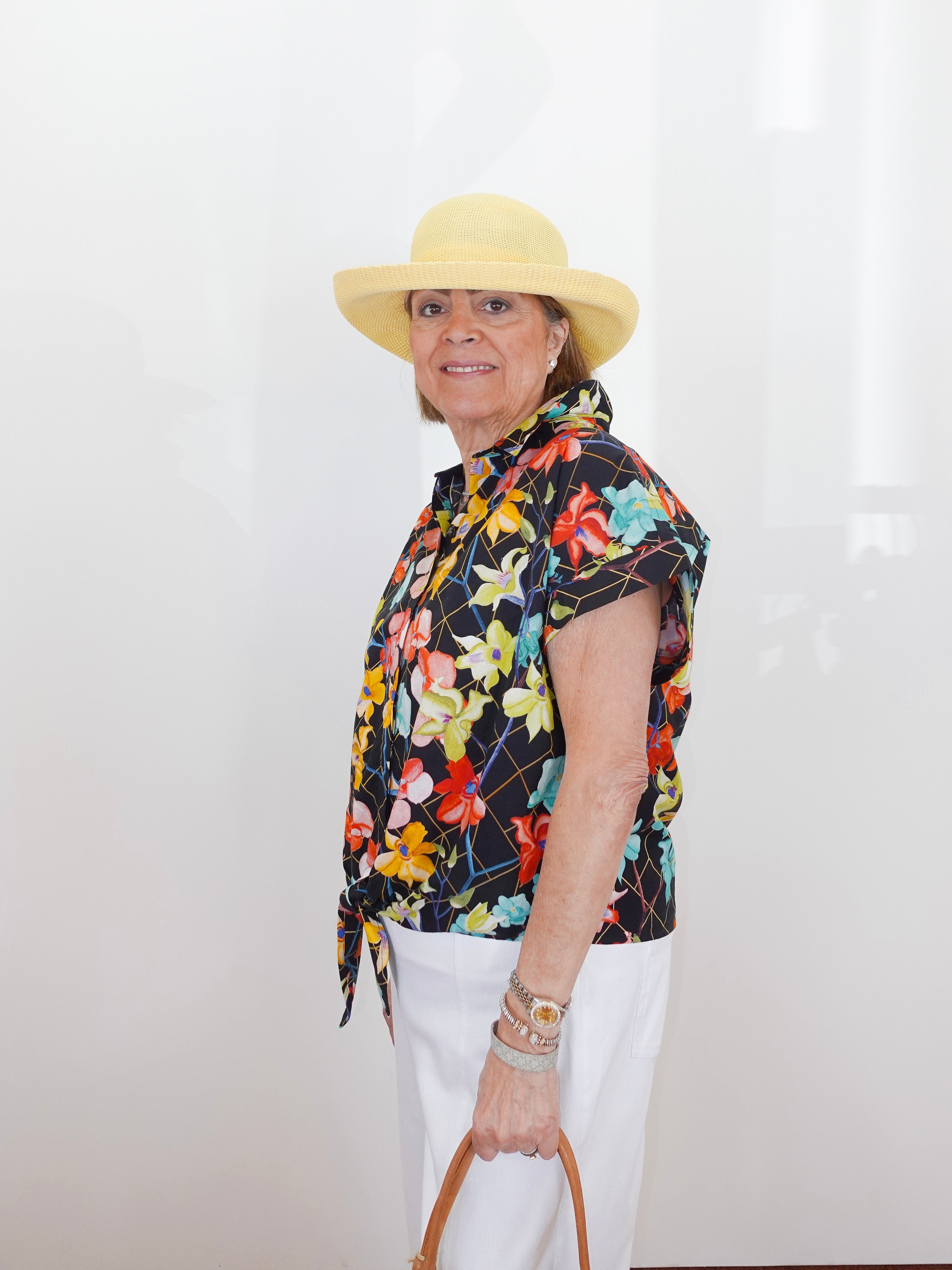 Person wearing a colorful floral shirt and white pants with a straw hat against a plain background