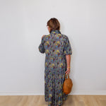 Person wearing a floral dress holding a brown bag against a white wall.