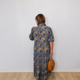 Person wearing a floral dress holding a brown bag against a white wall.