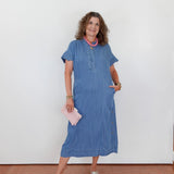 Woman in a blue dress standing against a white wall