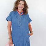 Woman wearing a blue dress with a pink clutch against a white background