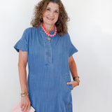 Woman wearing a blue dress with a pink clutch against a white background