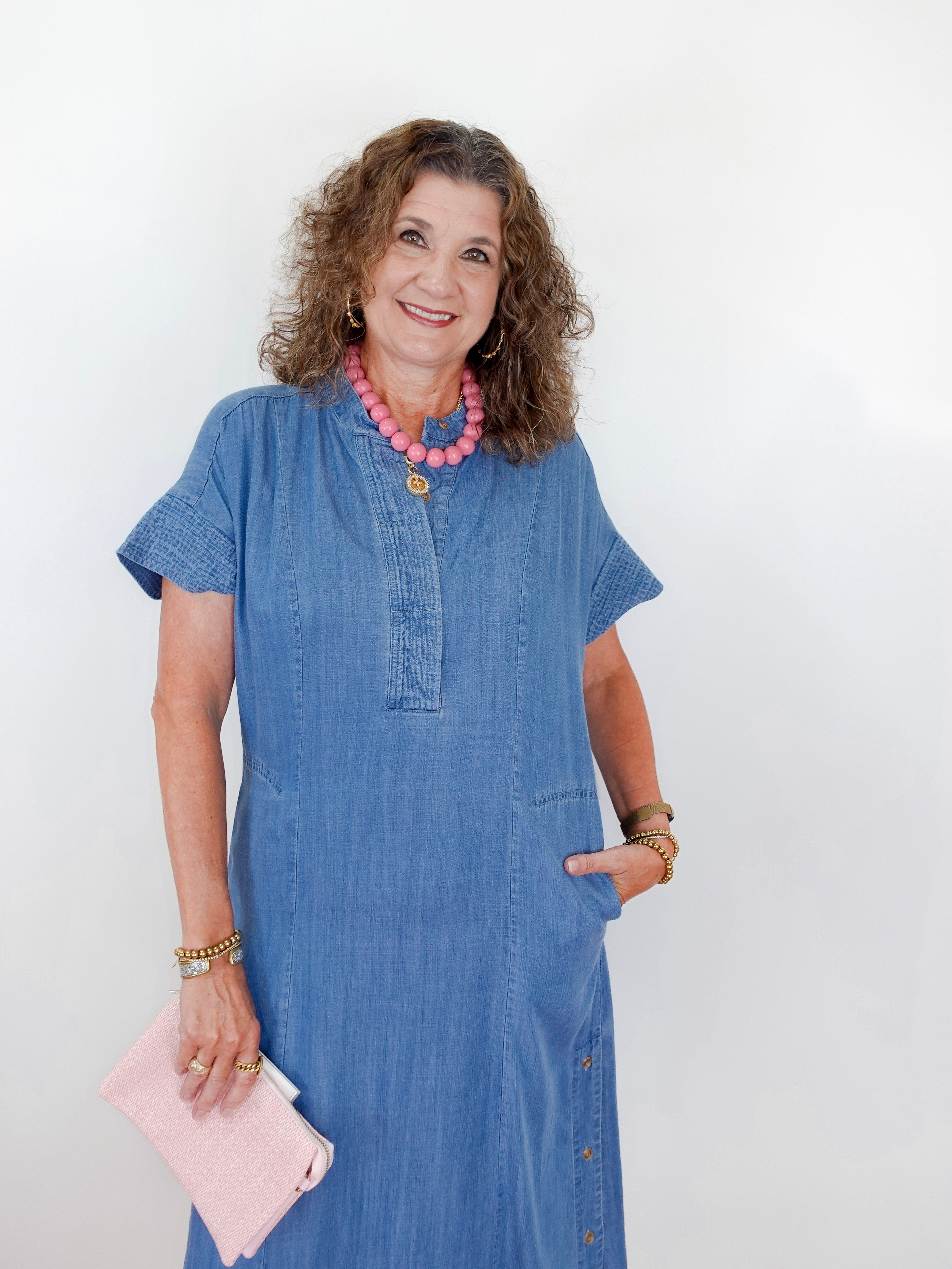 Woman wearing a blue dress with a pink clutch against a white background