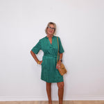 Woman wearing a green dress standing against a white wall.