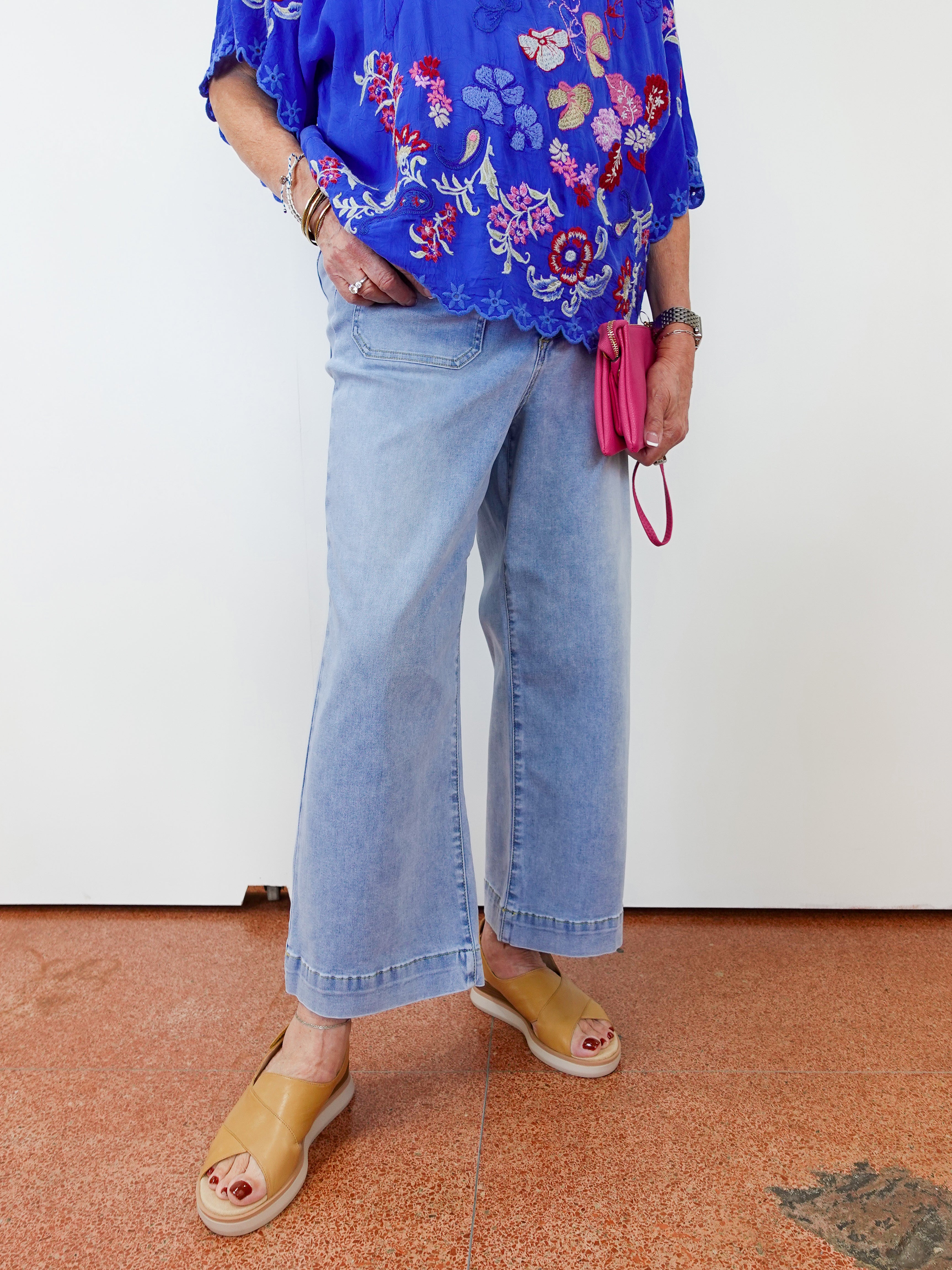 Person wearing a blue floral blouse, light blue jeans, and yellow sandals on a white background