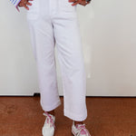Person wearing a striped shirt, white pants, and white sneakers with pink laces on a plain background.