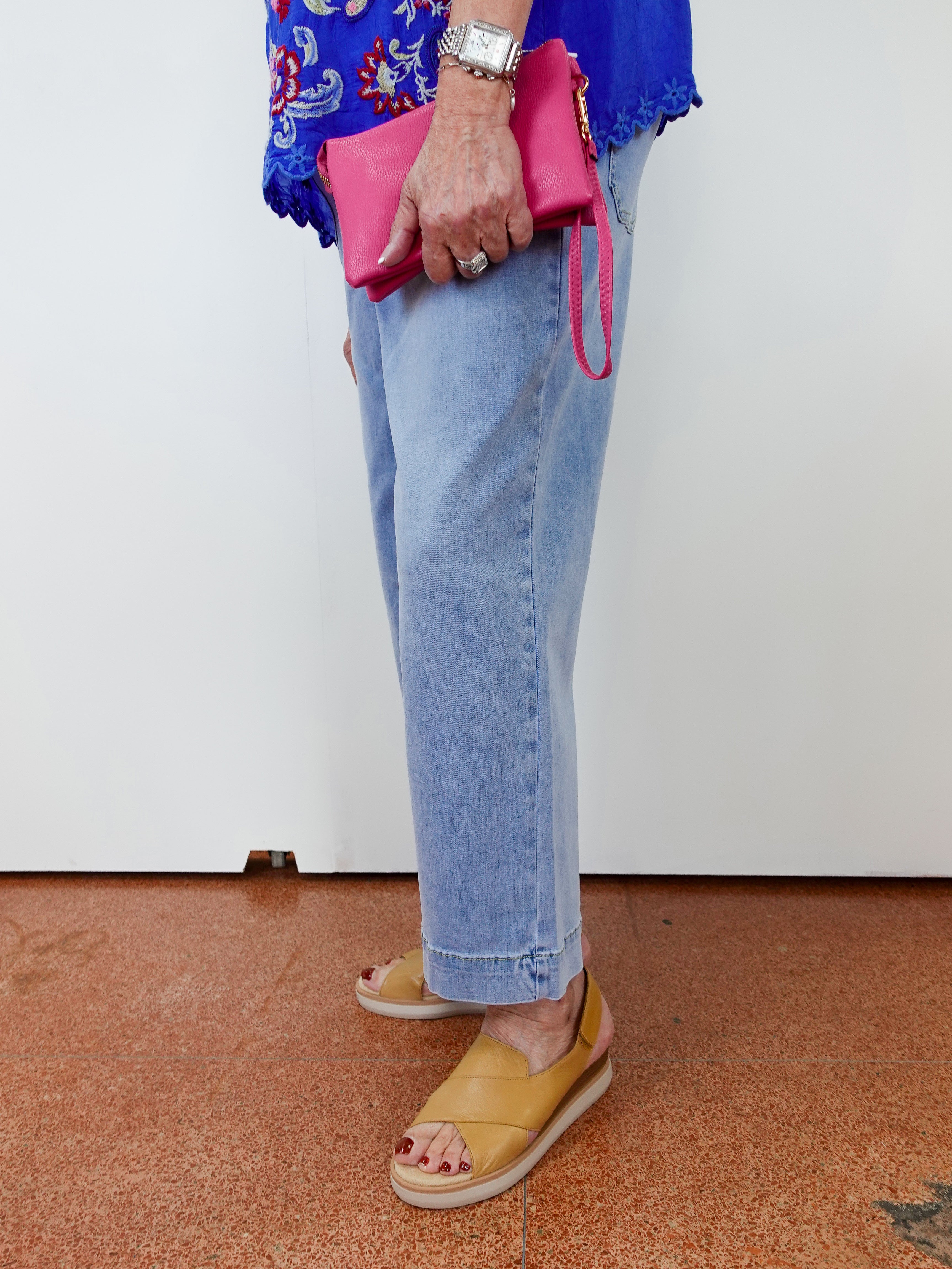 Person wearing blue jeans, yellow sandals, and holding a pink clutch against a white background