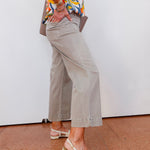 Person wearing a colorful shirt, beige pants, and sandals on a white wall background