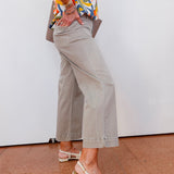 Person wearing a colorful shirt, beige pants, and sandals on a white wall background