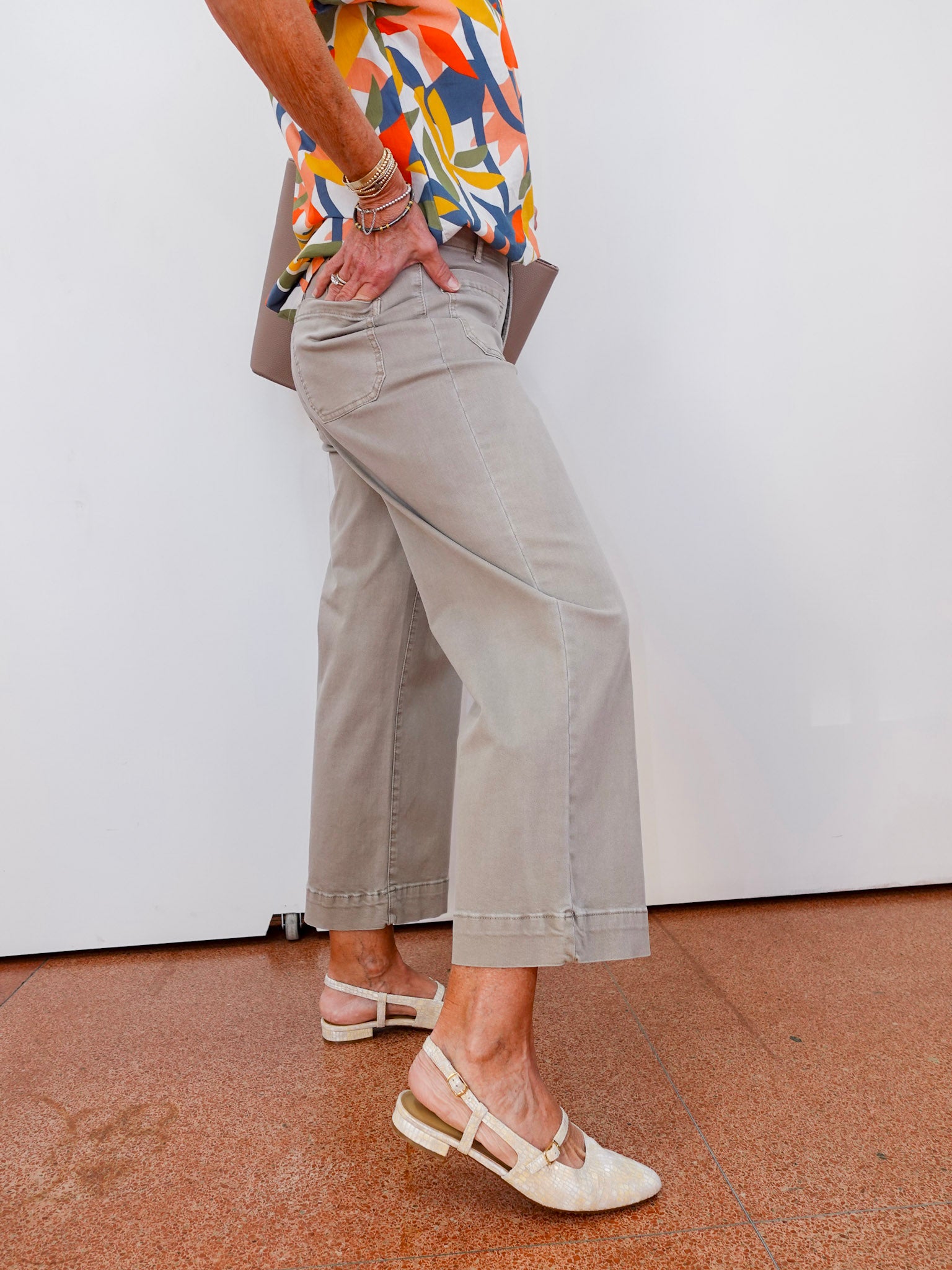 Person wearing a colorful shirt, beige pants, and sandals on a white wall background