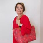 Woman in red shirt holding a large red patterned bag against a white wall