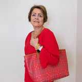Woman in red shirt holding a large red patterned bag against a white wall