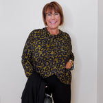 Woman wearing a leopard print top and black pants against a white wall