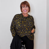 Woman wearing a leopard print top and black pants against a white wall